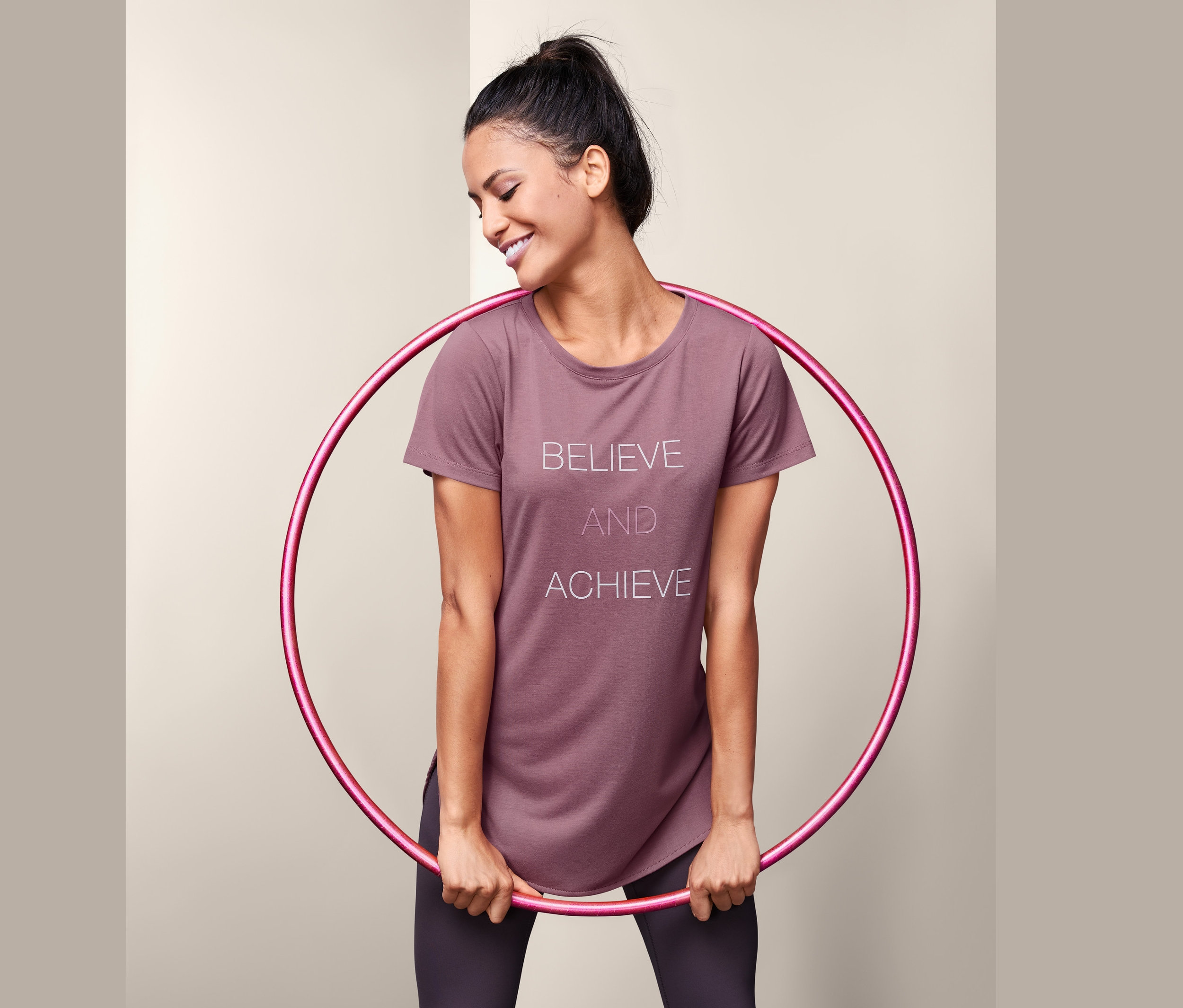 Frau hält Hula-Hoop-Reifen und trägt ein Sportshirt mit Schriftzug.