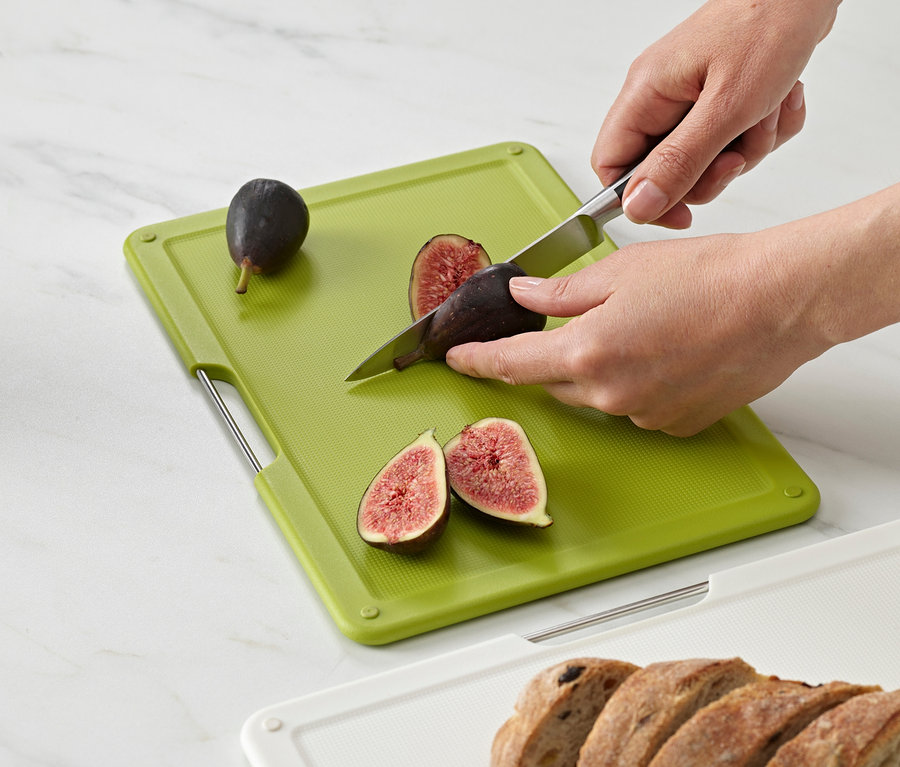 Person schneidet Feigen auf grünem Joseph Joseph Schneidebrett-Set »Folio Slim«.