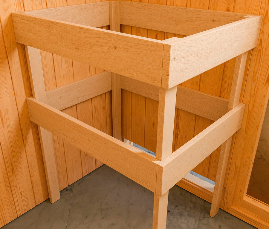 Holzkonstruktion der Karibu Fasssauna »Nadi 3« steht in einer Ecke des Raumes mit Holzverkleidung.