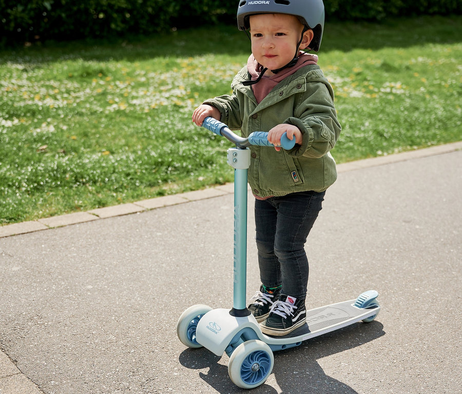 Kind mit Helm fährt blauen HUDORA Tri-Scooter.
