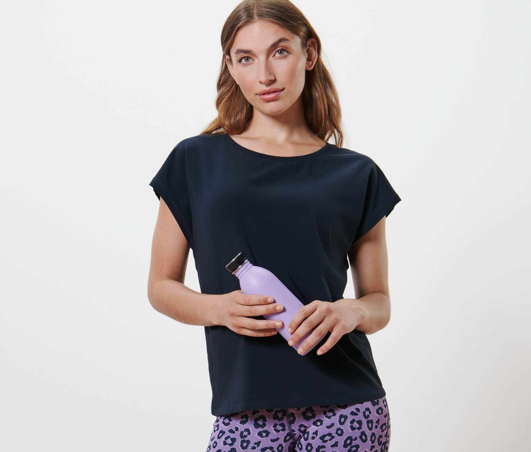 Frau hält eine lila Wasserflasche und trägt ein dunkelblaues Sportshirt.