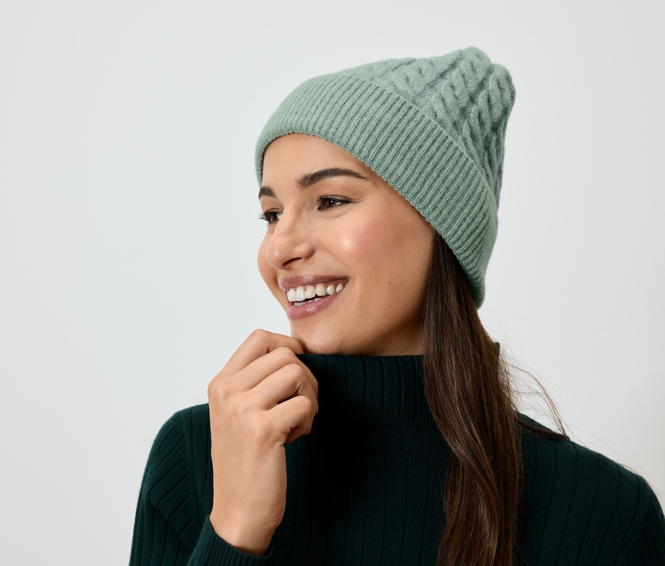 Lächelnde Frau mit braunem Haar, grüner Strickmütze und grünem Rollkragenpullover.