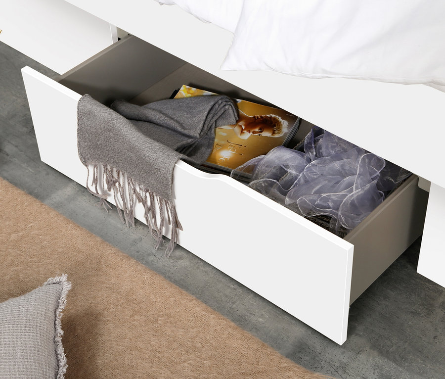 Offene Schublade eines weißen rauch Bettes "Aditio Beds" in 140 cm Größe, in der ein grauer Schal mit Fransen und verschiedene Gegenstände liegen.