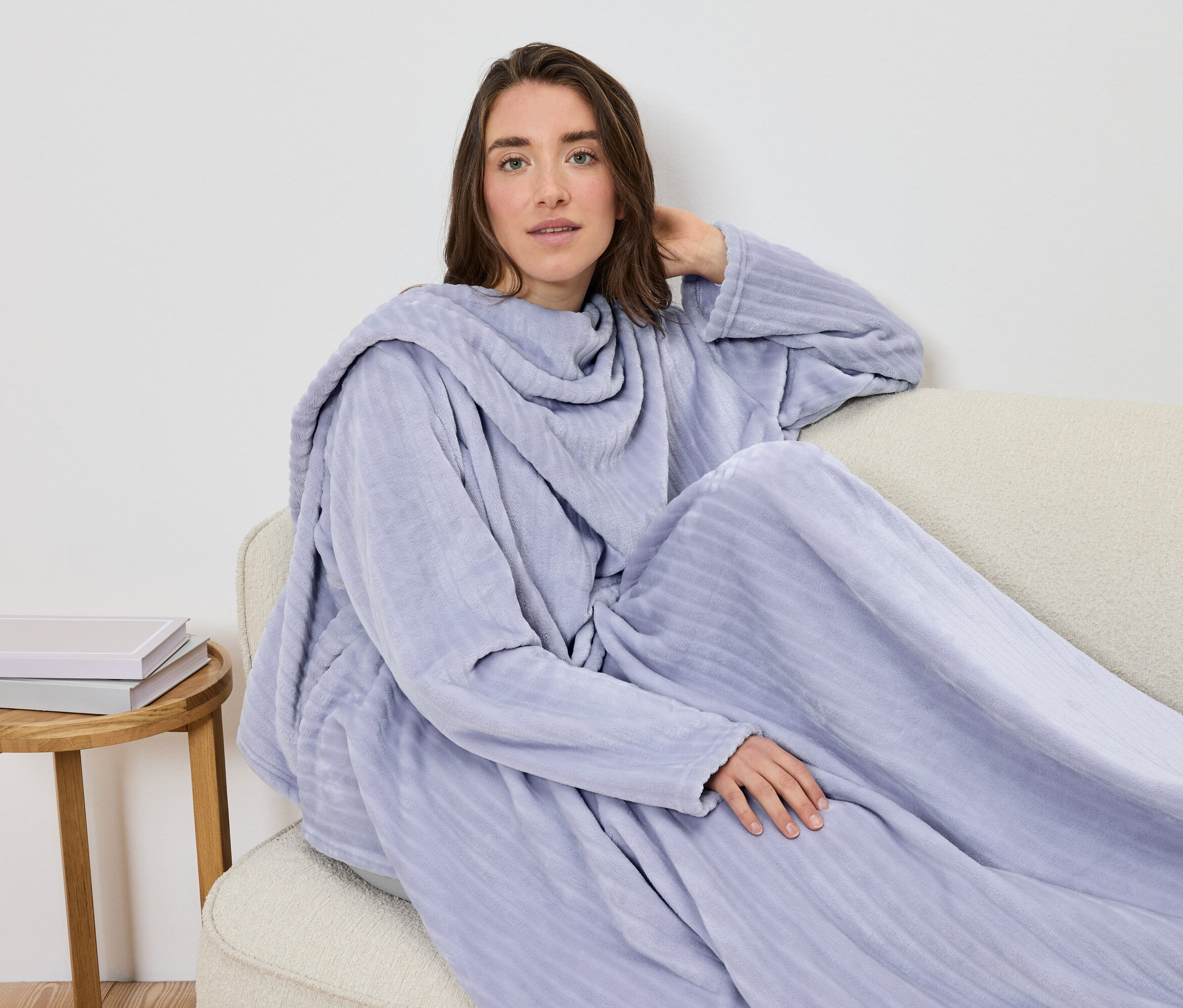 Eine Frau sitzt in eine hellviolette Ärmeldecke gehüllt auf einem Sofa.