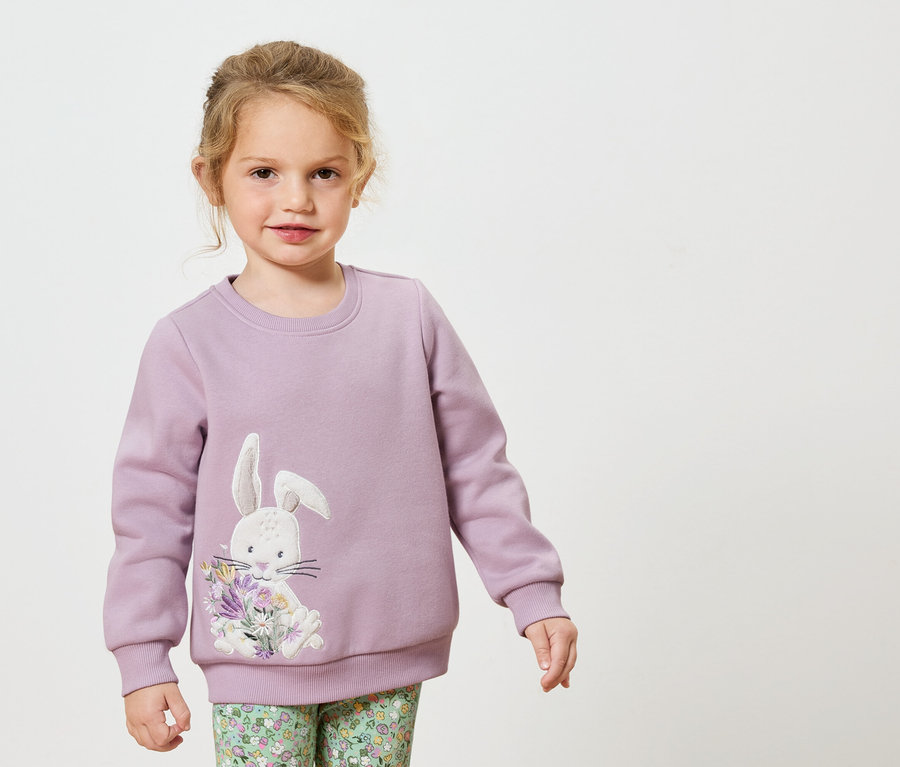 Mädchen trägt lila Sweatshirt mit Hasen- und Blumenapplikation.