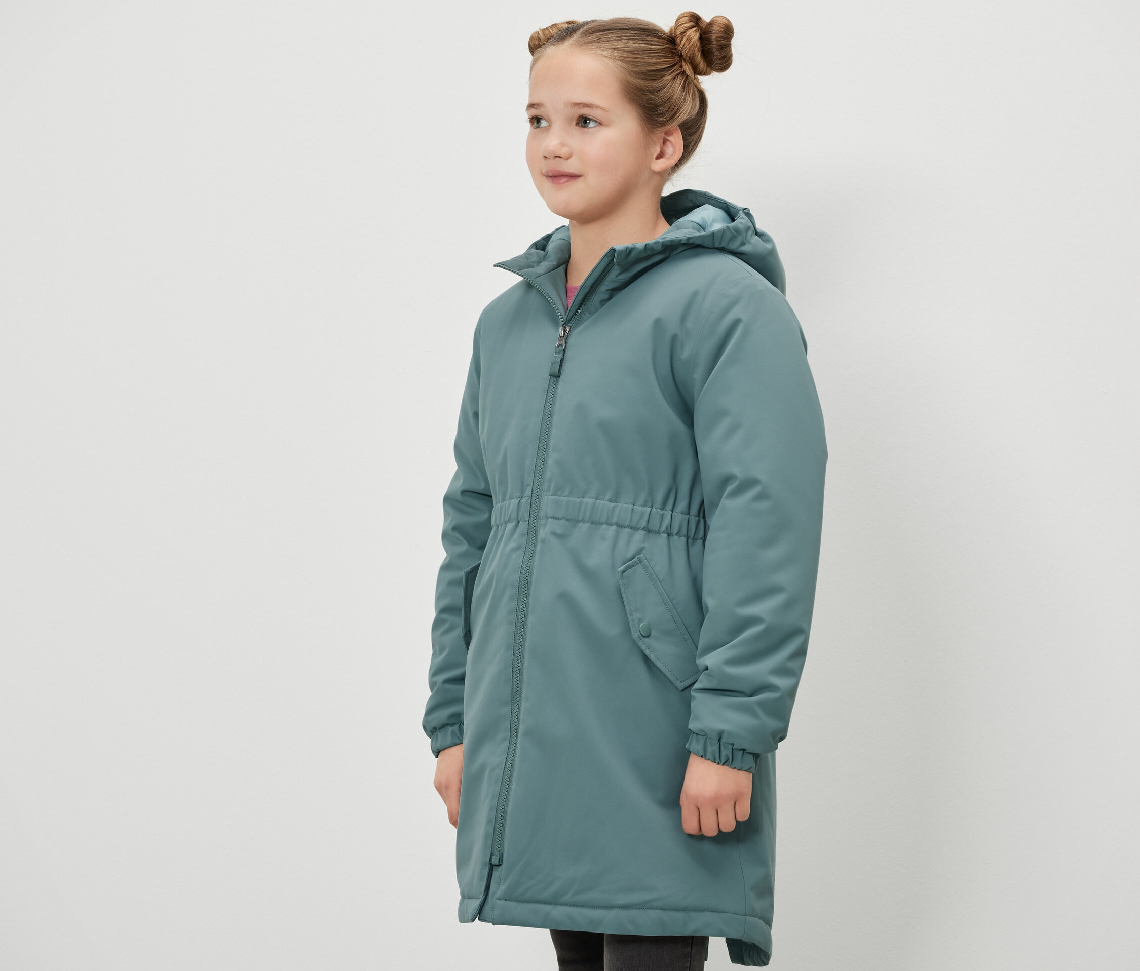 Mädchen steht seitlich und trägt eine grüne Kinder-Thermoparka.