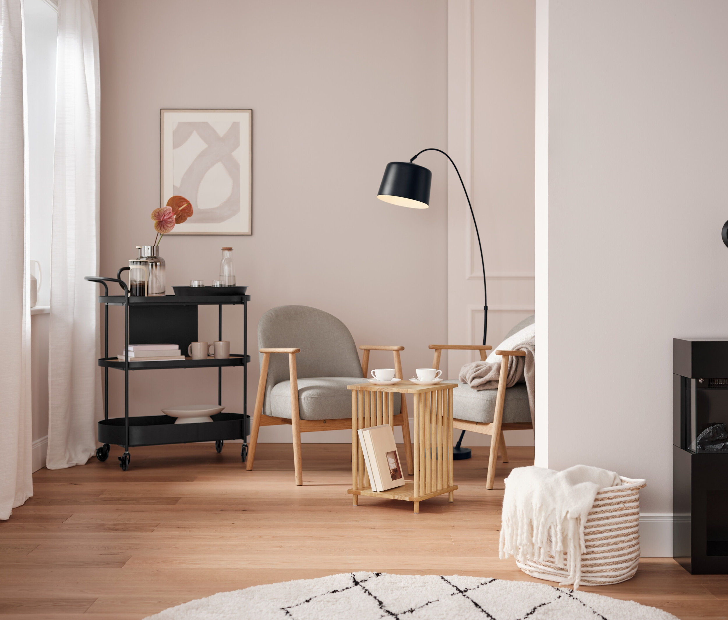 Wohnzimmer mit schwarzem Servierwagen, zwei grauen Sesseln und einem schwarzen Kamin.