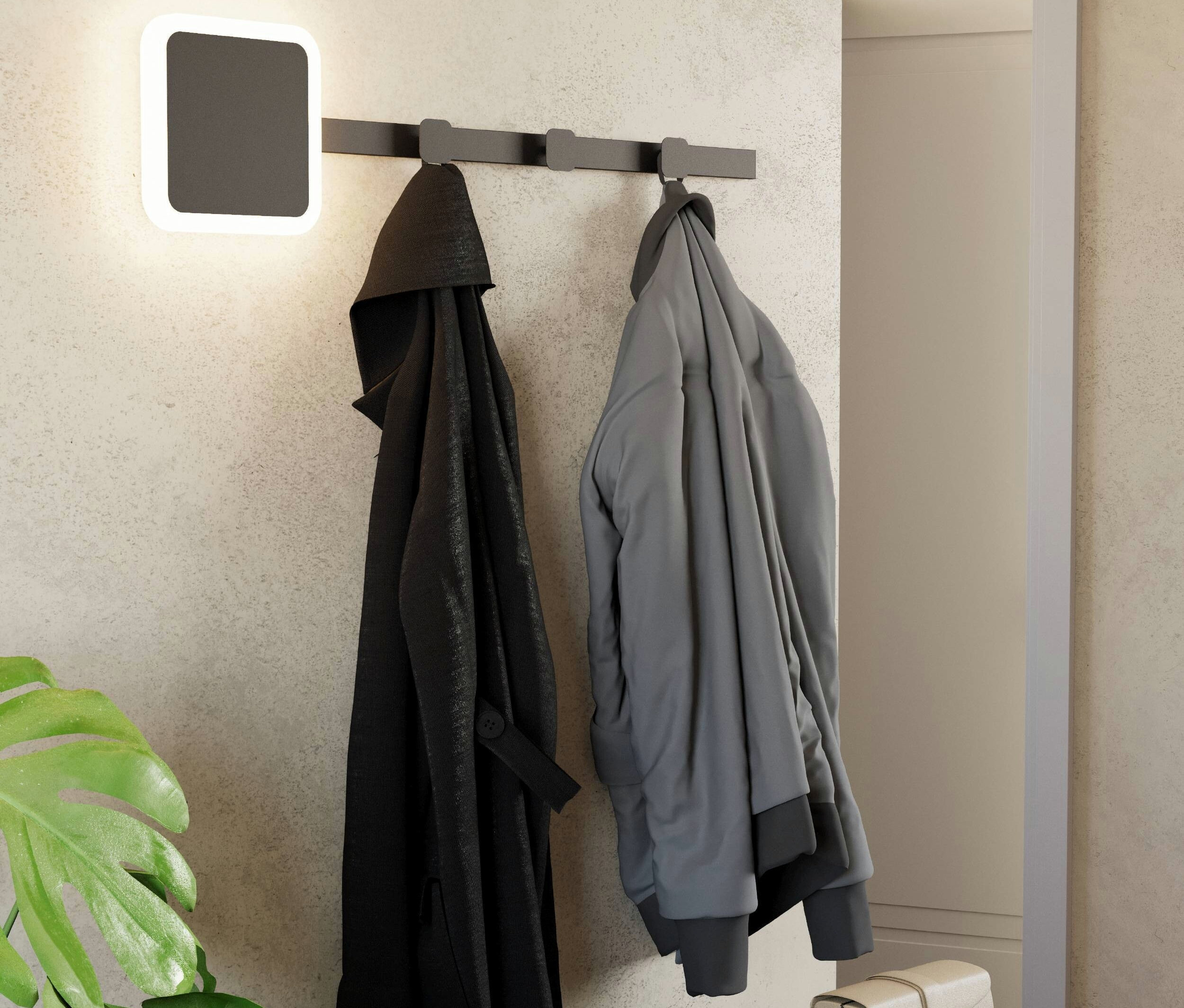 Eine schwarze Jacke und eine graue Jacke hängen an einer Garderobe neben einer quadratischen Lampe an der Wand.
