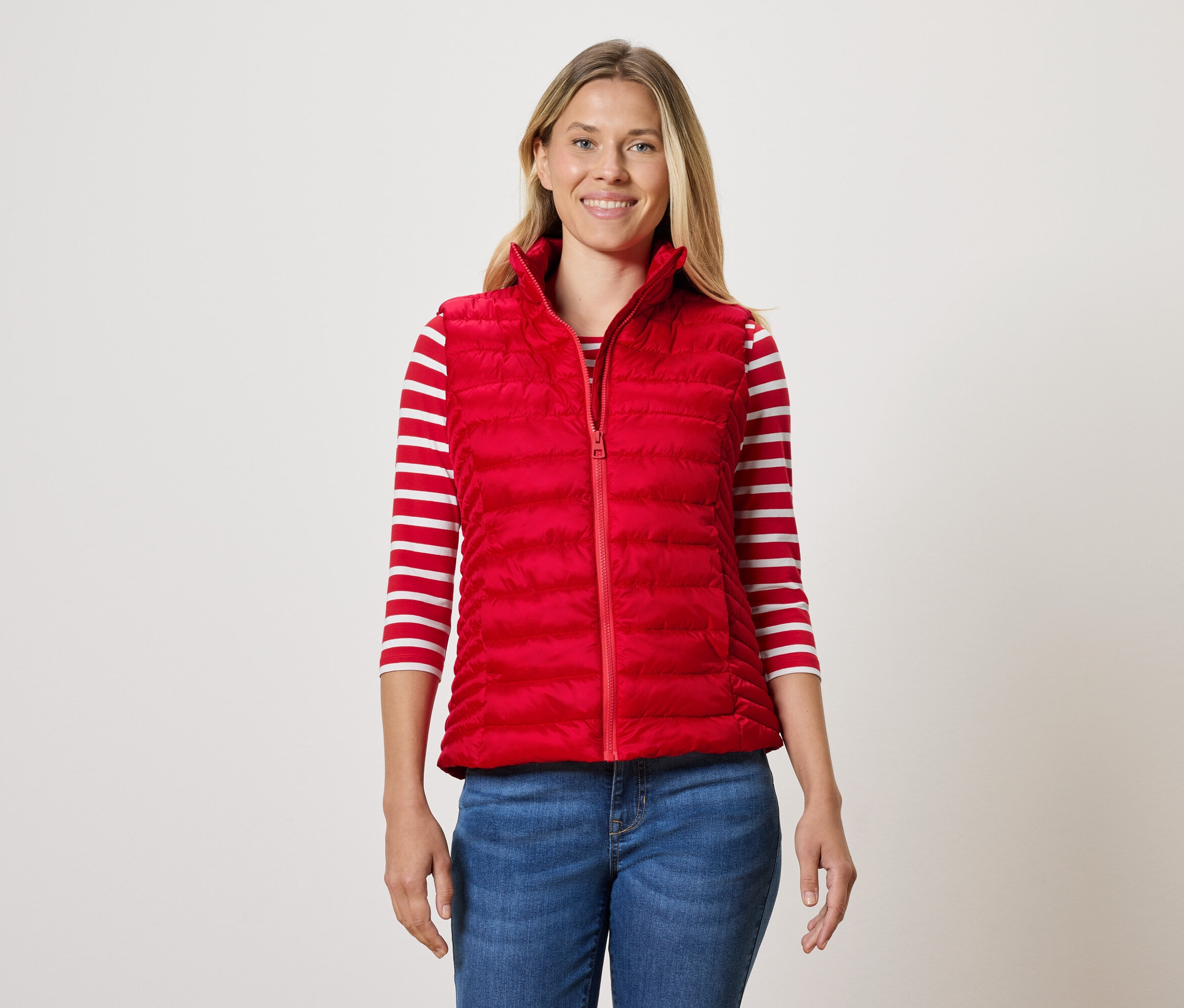 Frau trägt eine rote Steppweste, ein gestreiftes T-Shirt und Jeans.