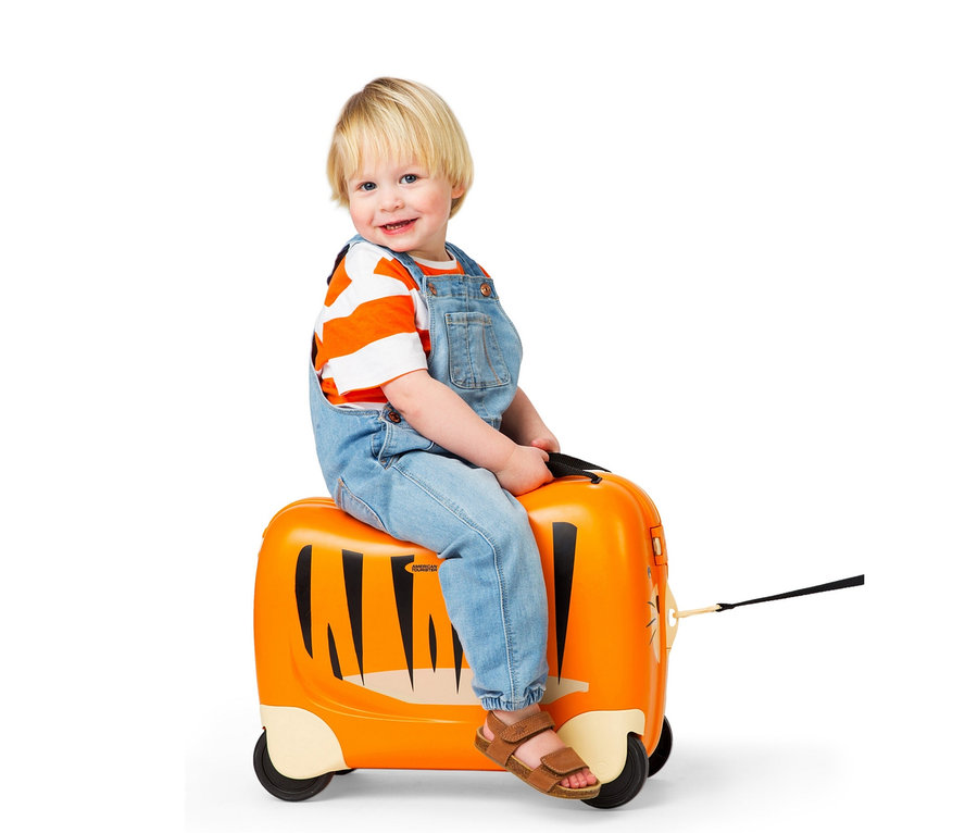 Ein Junge sitzt auf einem orangefarbenen Koffer mit Tigermuster und Rädern.