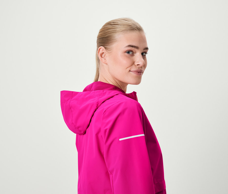 Blonde Frau blickt über die Schulter und trägt eine pinke Kapuzenjacke.