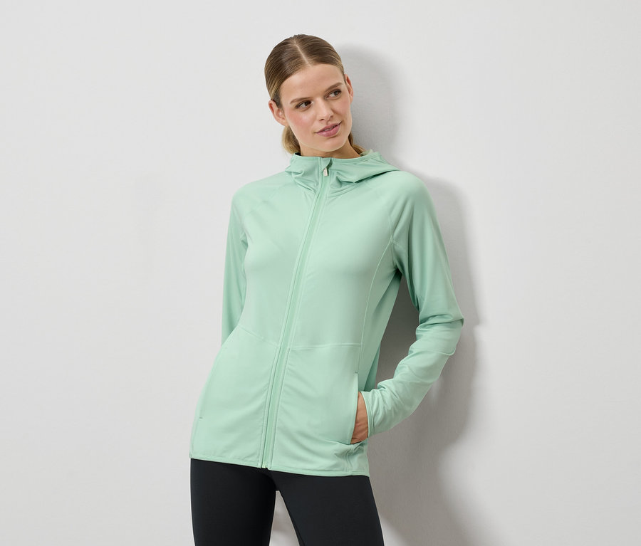 Frau posiert in mintgrüner Kapuzenjacke und schwarzen Leggings.