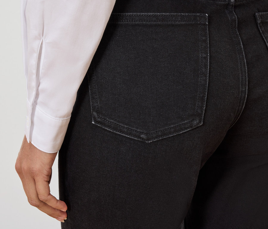 Detailansicht der Rückseite von schwarzen Jeans an einer Person mit einem weißen Hemd.