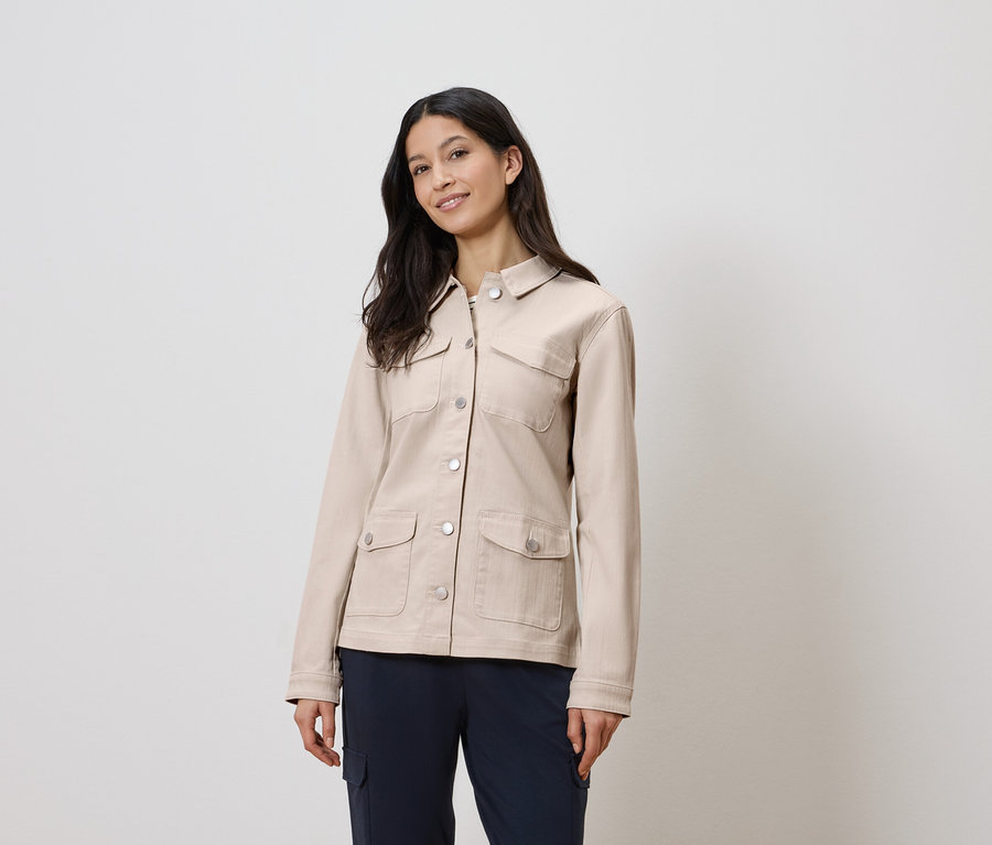 Frau trägt eine beige Jacke und blaue Hose.