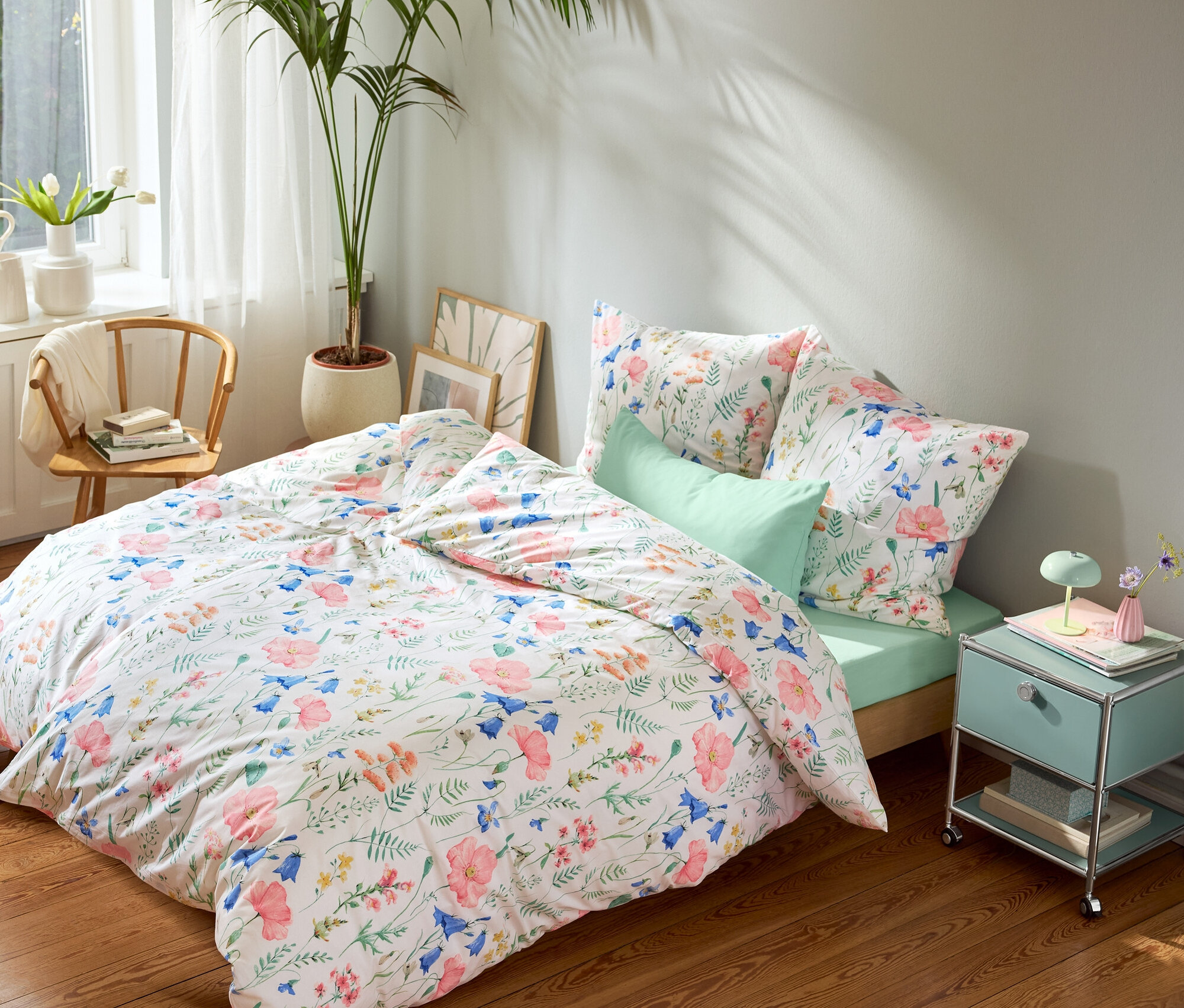 Bett mit blumengemusterter Bettwäsche, mintgrünem Spannbettlaken und mintgrünen Kissenbezügen, einem mintgrünen Nachttisch und einem runden Teppich.