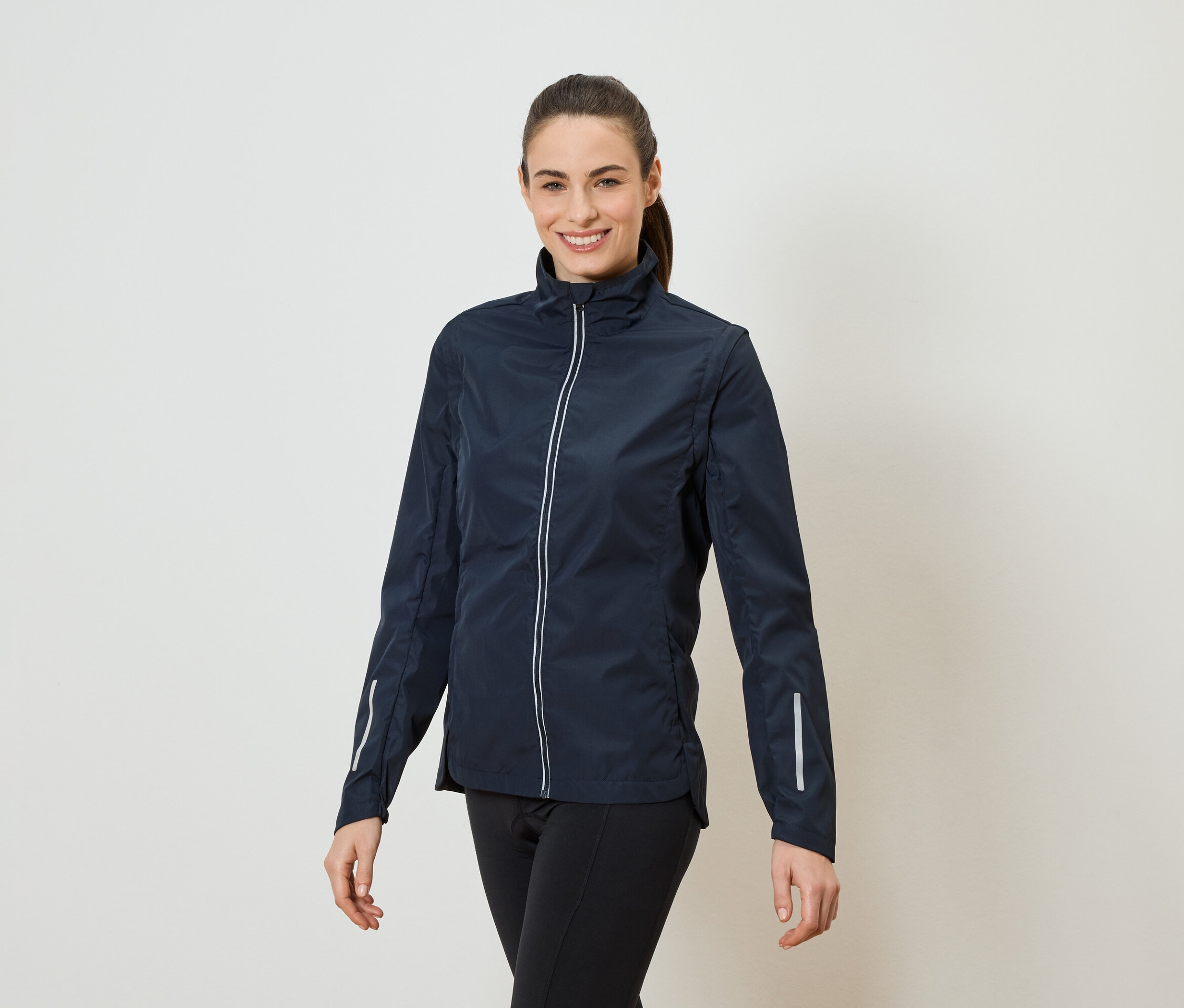 Eine Frau mit Pferdeschwanz trägt eine marineblaue Jacke mit durchgehendem Reißverschluss und schwarzen Leggings.
