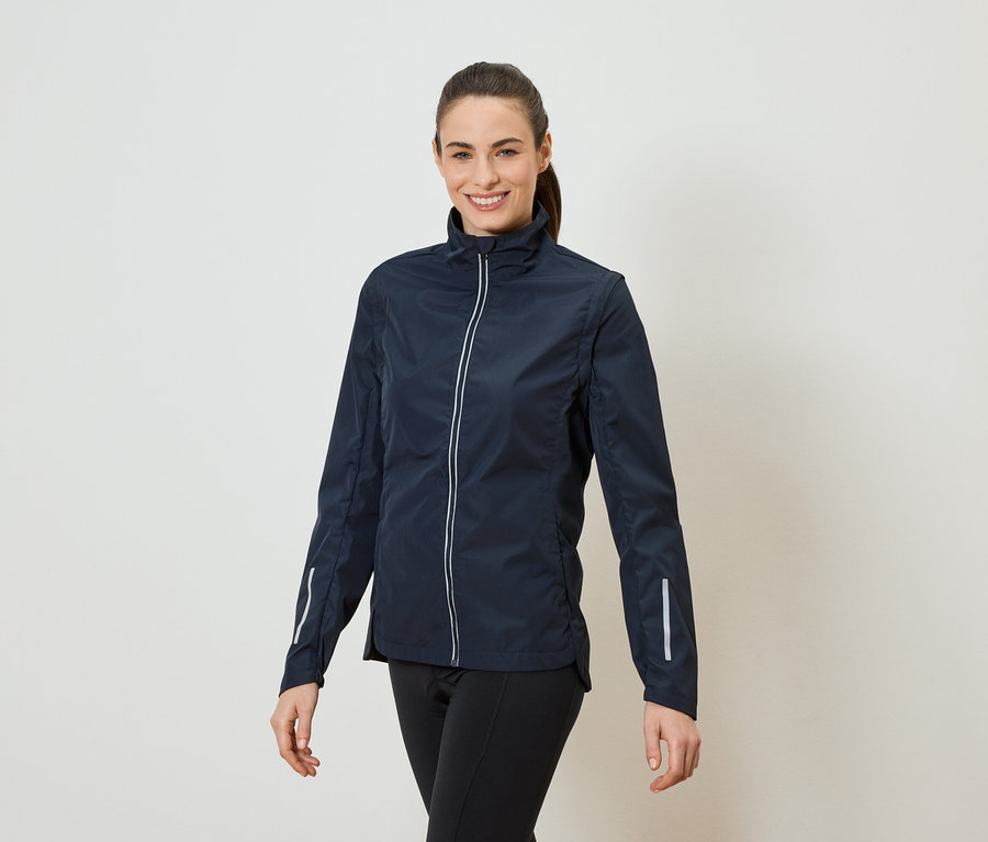 Eine Frau mit Pferdeschwanz trägt eine marineblaue Jacke mit durchgehendem Reißverschluss und schwarzen Leggings.