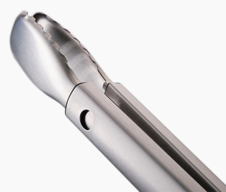 Detailaufnahme einer silbernen Grillzange vor einem weißen Hintergrund.