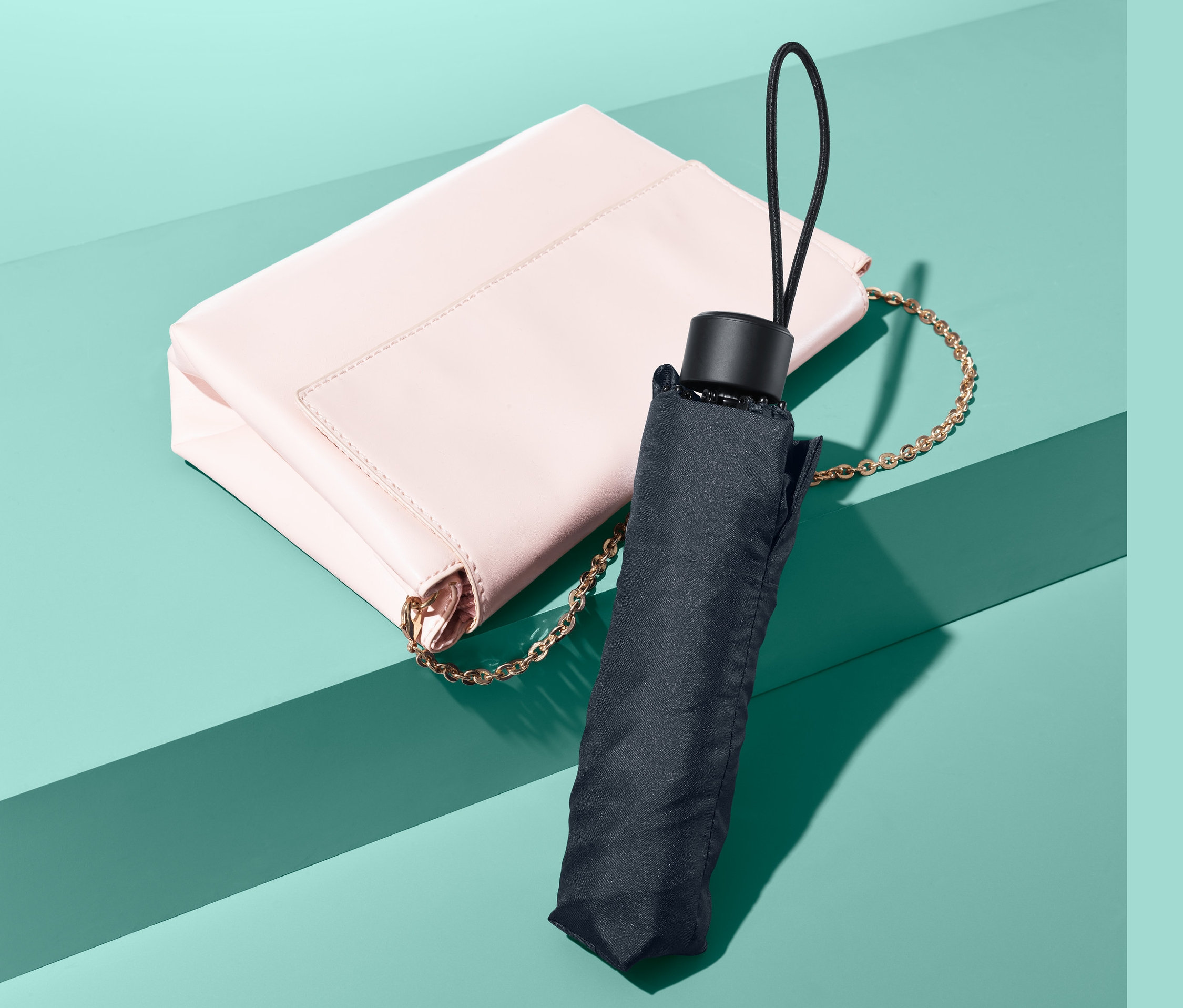 Eine rosa Handtasche mit einem Mini-Regenschirm daneben.