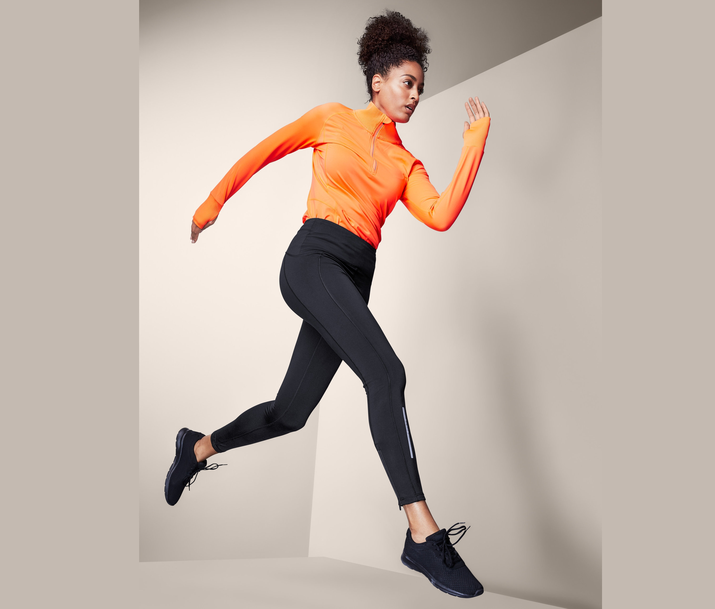 Frau in orangefarbenem Oberteil und schwarzen Thermo-Lauftights springt.