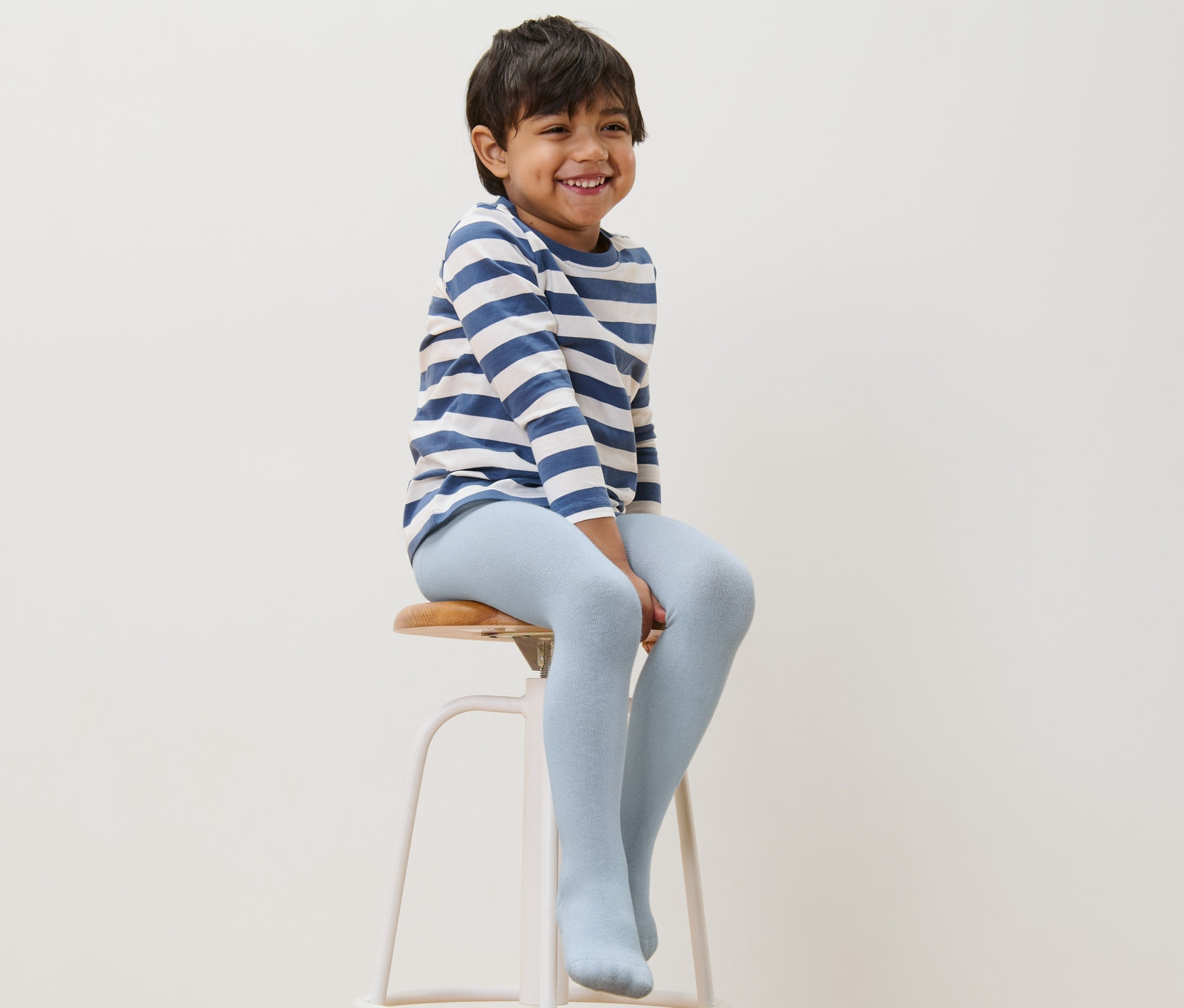 Ein Junge sitzt auf einem Hocker und trägt eine blaue Baumwollstrumpfhose.