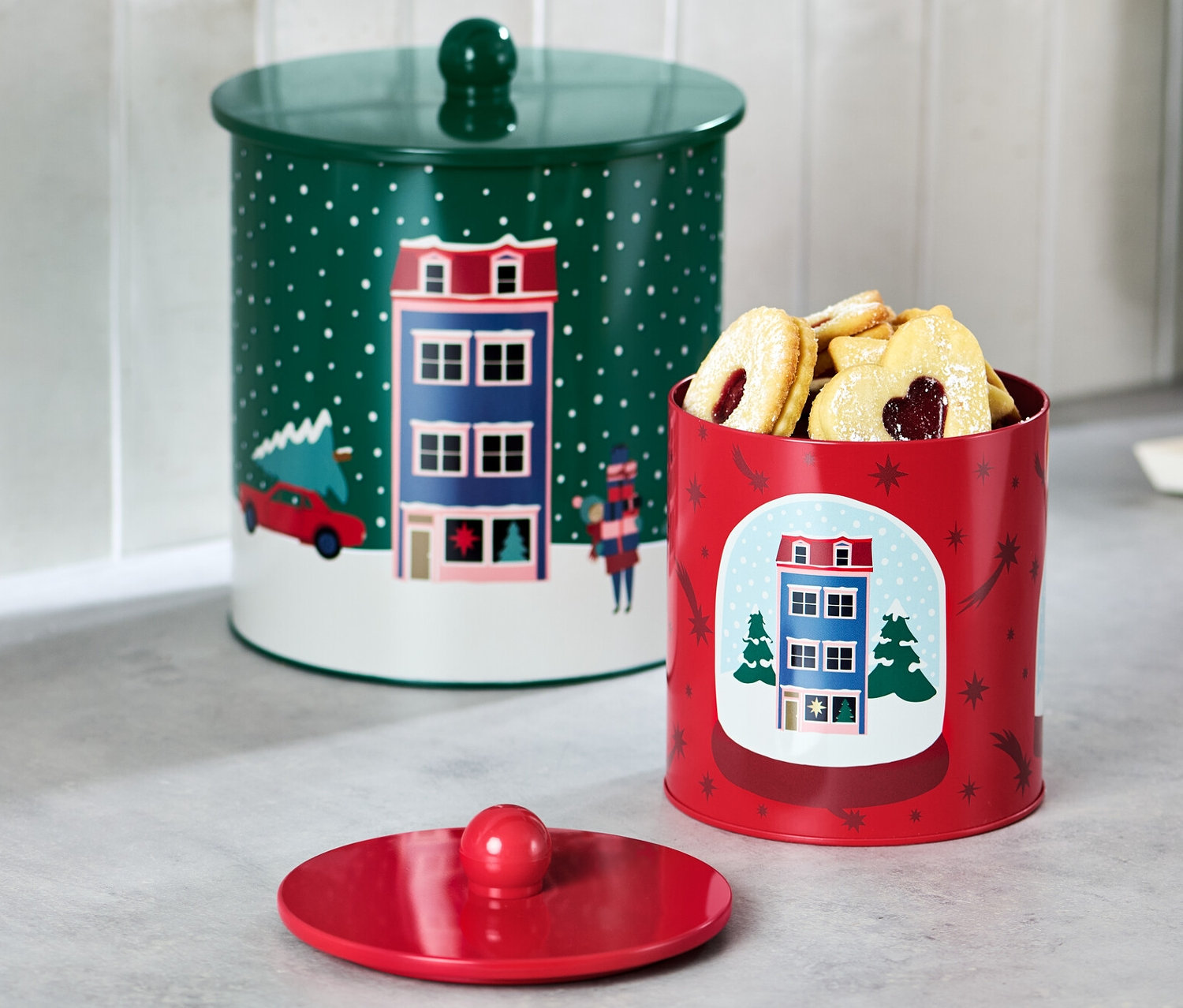 Zwei Keksdosen stehen auf einer Küchentheke. Eine Dose ist grün mit Deckel, die andere rot und mit Keksen gefüllt.