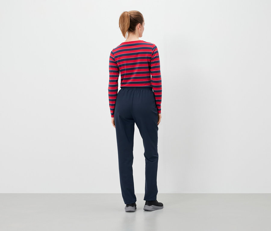 Rückansicht einer Frau mit braunen, zu einem Pferdeschwanz zusammengebundenen Haaren, die ein rot-blau gestreiftes Langarmshirt und eine dunkelblaue Hose trägt.