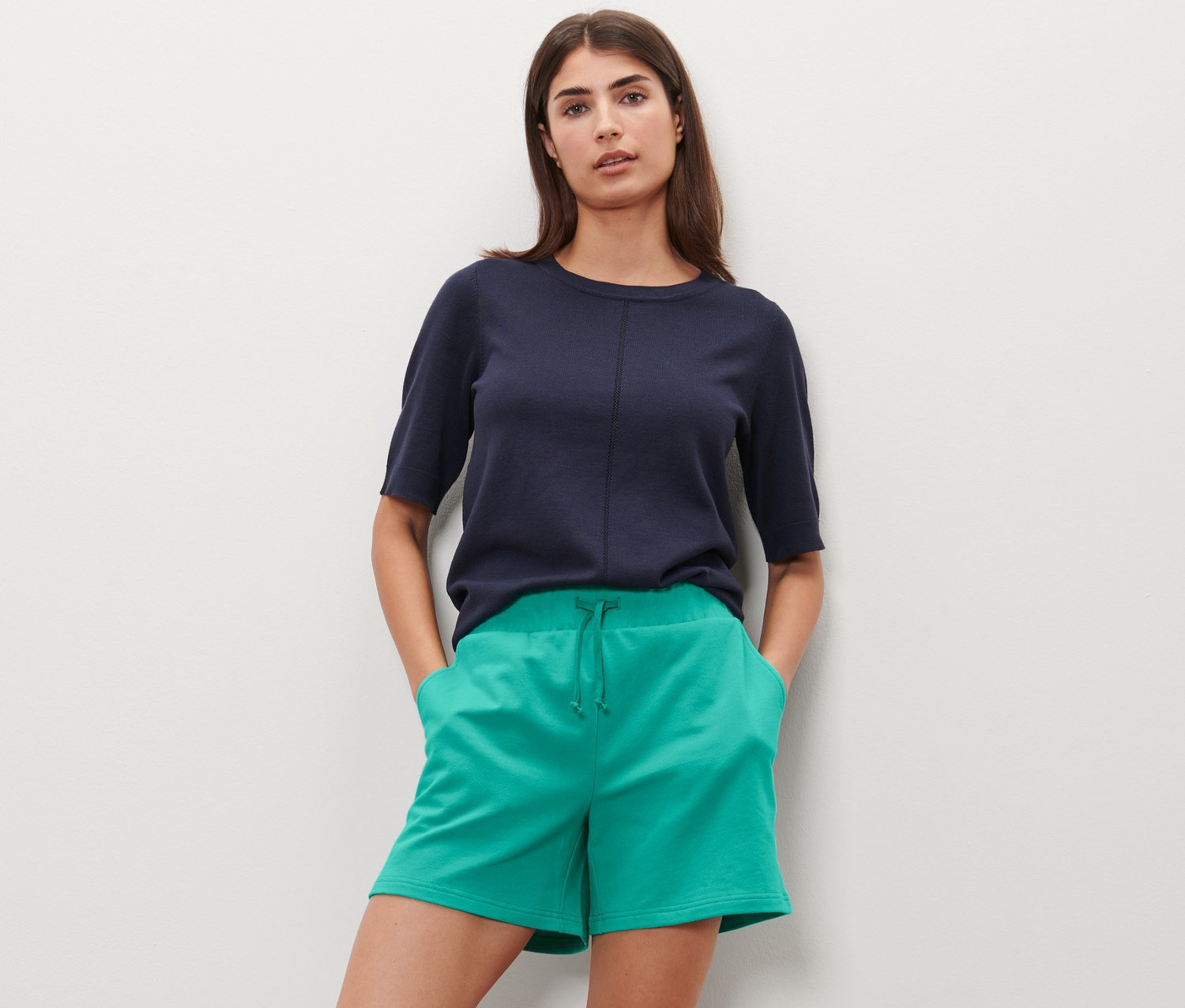 Frau posiert mit Händen in den Taschen der aquafarbenen Sweatshorts.