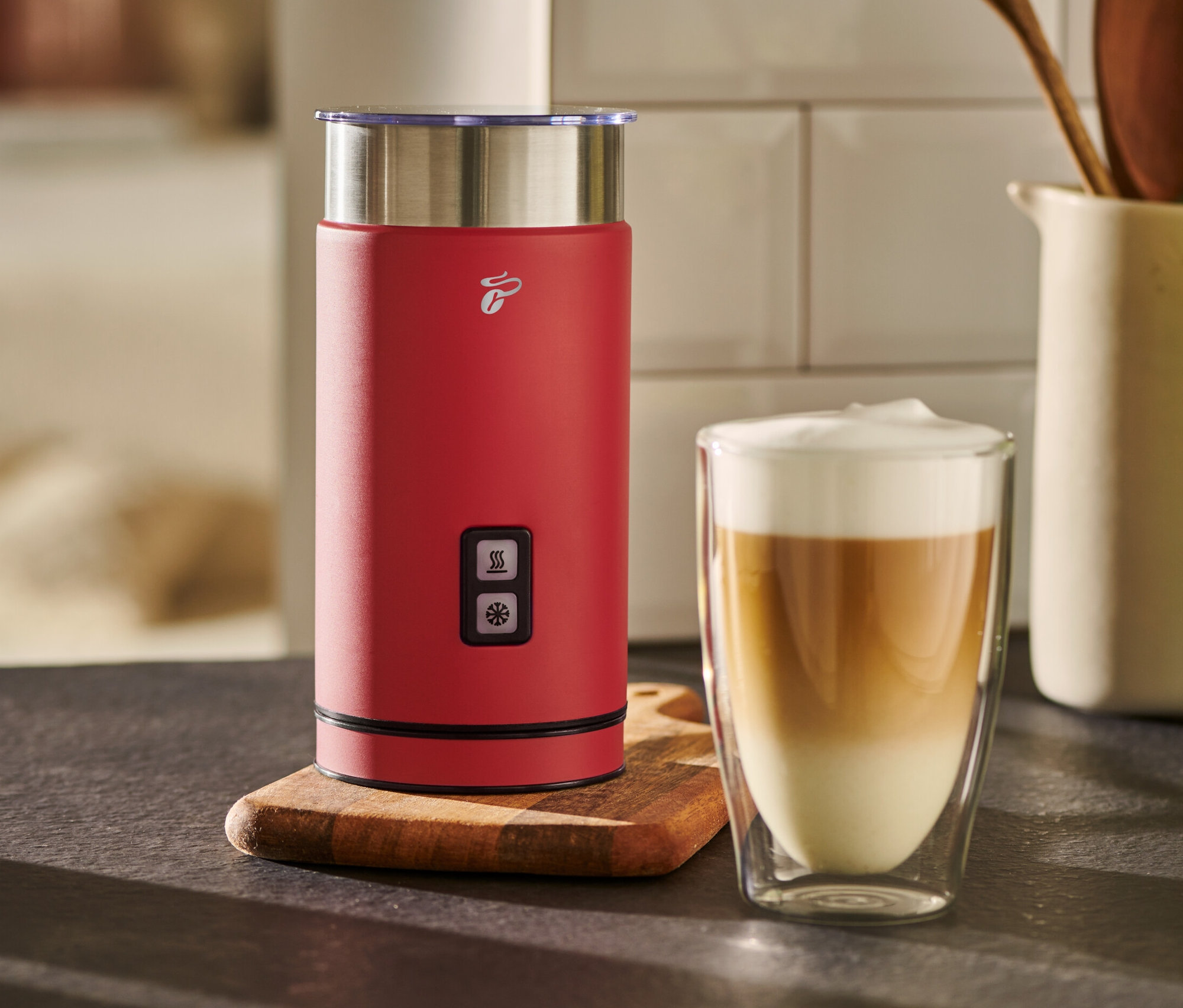 Ein roter elektrischer Milschaufschäumer steht neben einem Glas mit Kaffee und Milch.