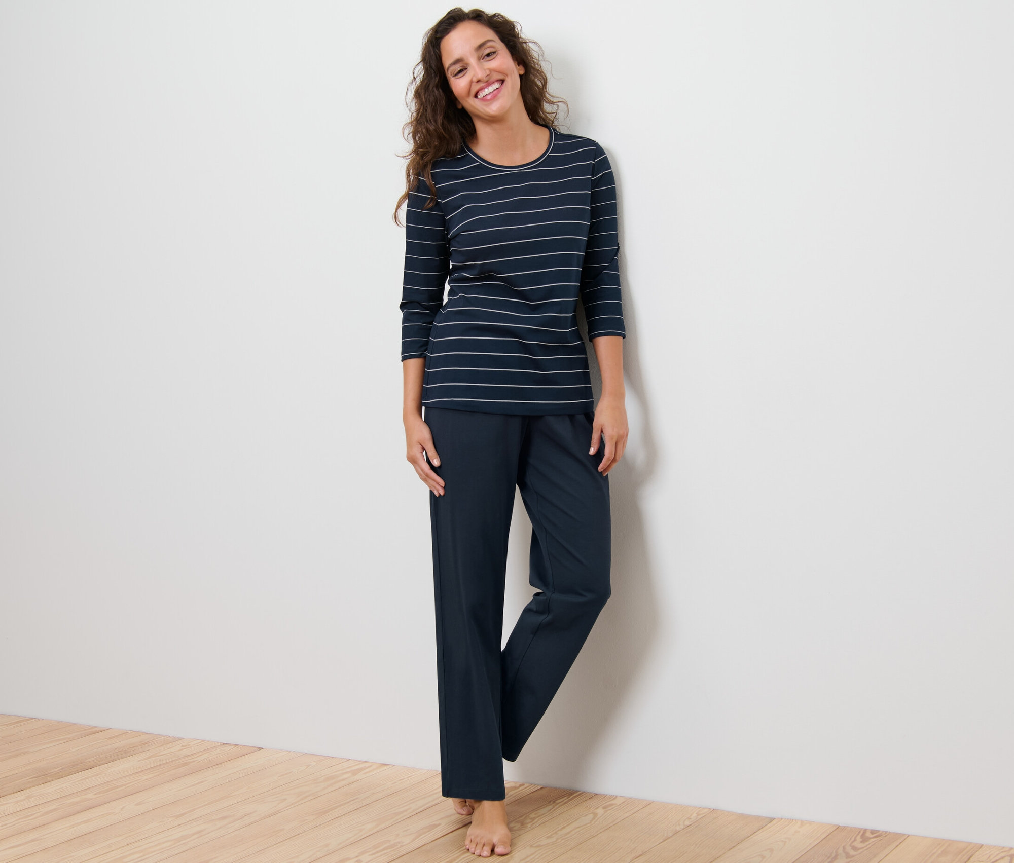 Frau steht und trägt einen Pyjama mit Streifen.