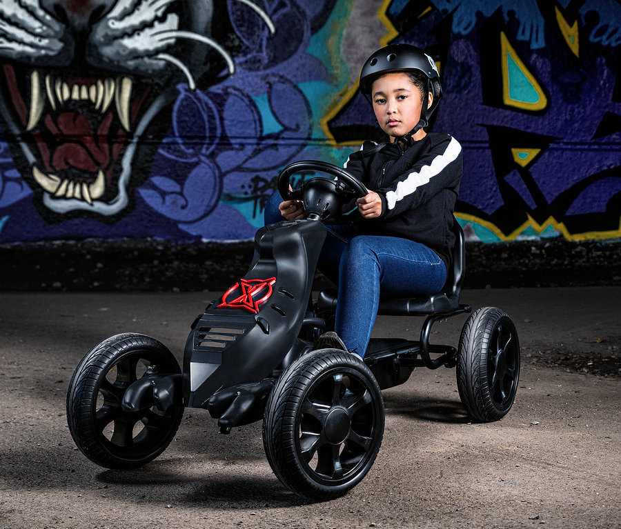 Mädchen mit Helm sitzt in schwarzem Xootz Gokart »Venom« vor einer Graffiti-Wand.