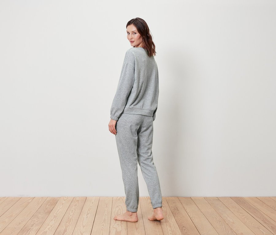 Eine Frau blickt über ihre Schulter und trägt ein graues Set aus Sweatshirt und Jogginghose.