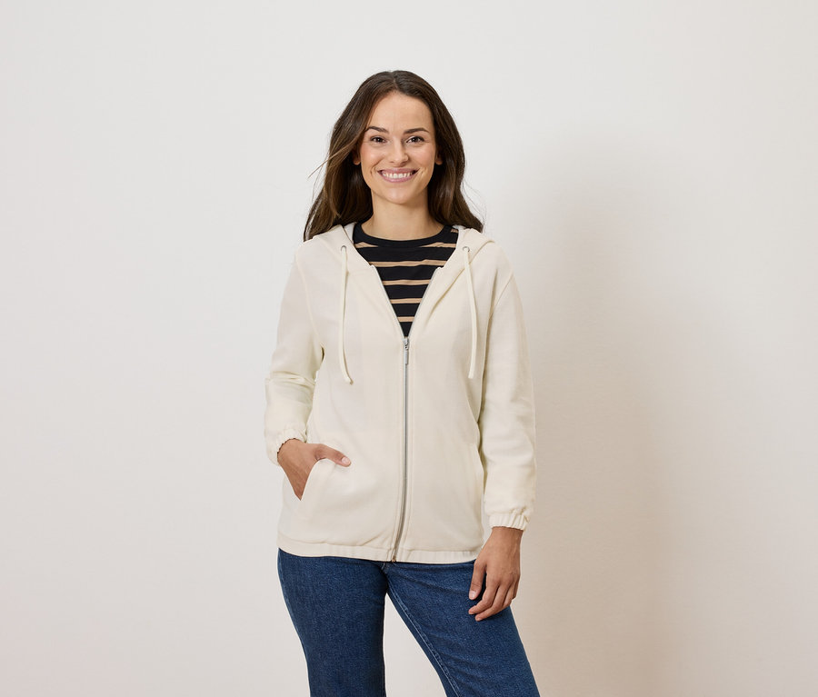 Frau posiert in cremefarbener Zip-Hoodie und blauen Jeans.