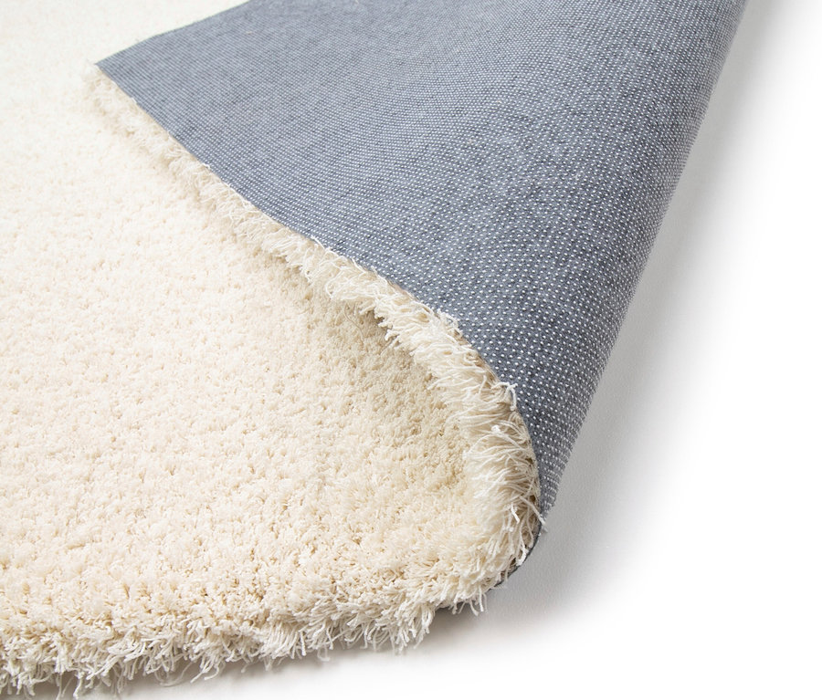 Nahaufnahme eines cremefarbenen Teppichs »Pleasure« mit den Maßen 200 x 290 cm, 80 x 150 cm, 120 x 170 cm und 160 x 230 cm, der aufgerollt ist und die Unterseite zeigt.