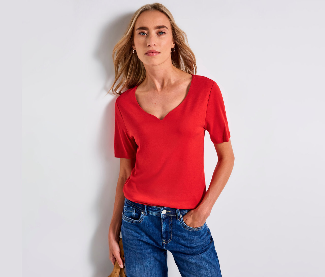Frau trägt ein rotes Street One Shirt mit Herzausschnitt und blaue Jeans.