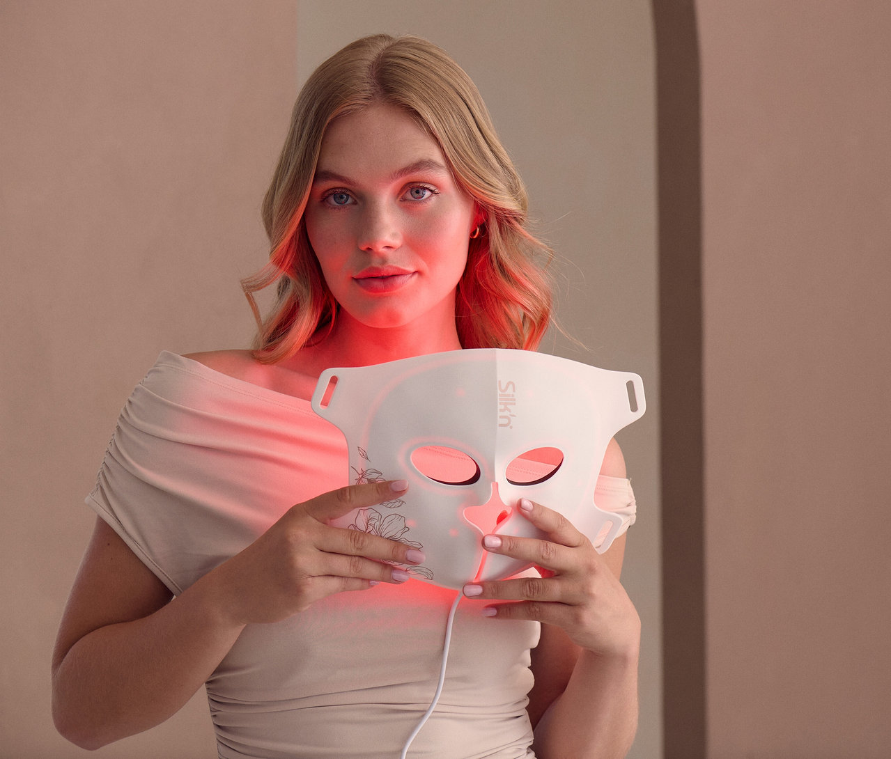 Frau hält Silk'n LED Gesichtsmaske mit EMS vor ihr Gesicht.