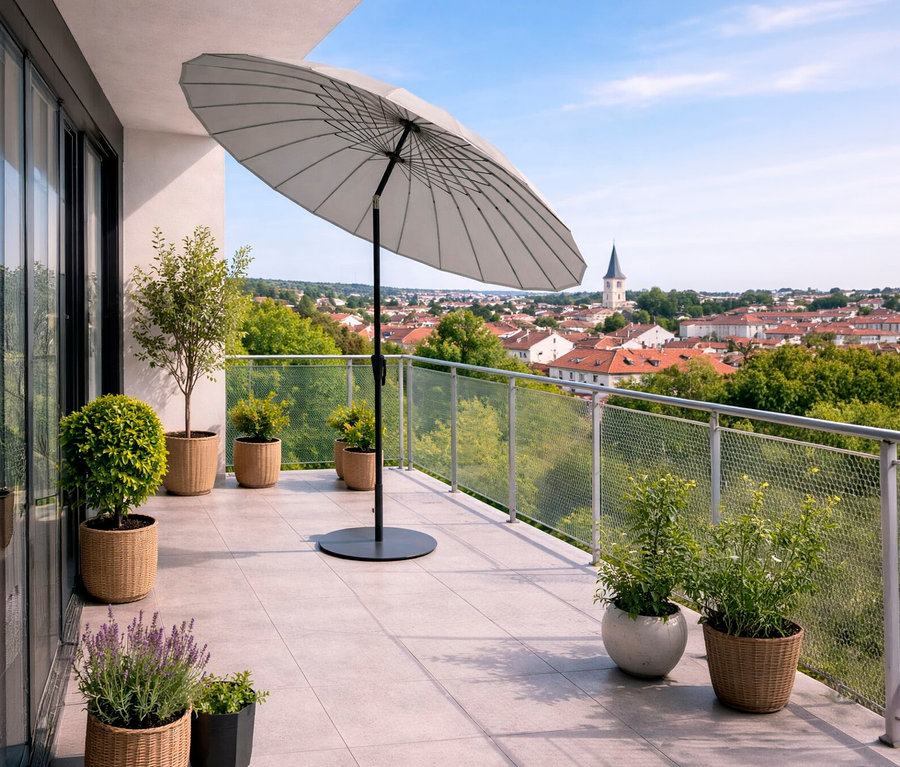 Auf einer Terrasse steht ein hellgrauer Leco Shanghai Sonnenschirm (Ø 270 cm) neben mehreren Pflanzen in Töpfen mit Blick auf eine Stadt.