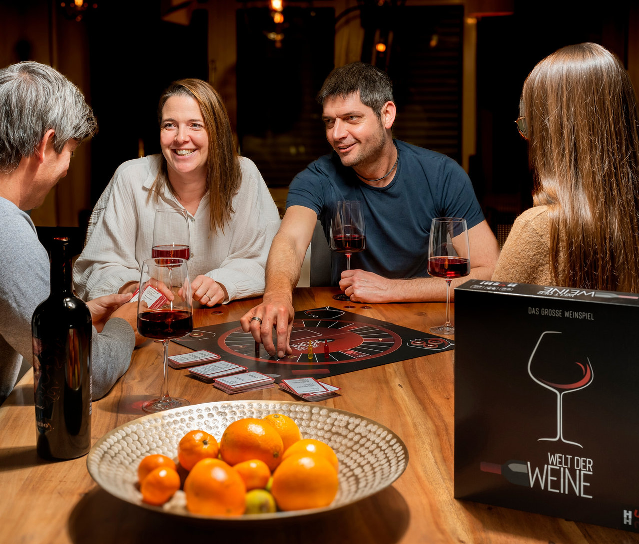 Vier Personen sitzen am Tisch und spielen das Spiel »Welt der Weine«.
