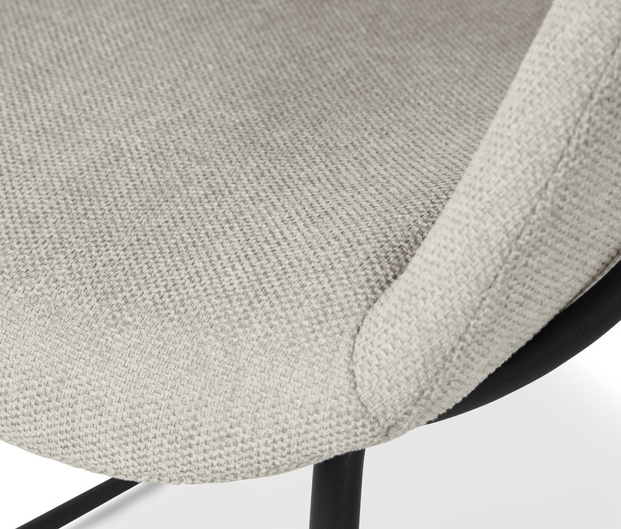 Detailansicht eines beige gepolsterten Schalenstuhls mit Metallbeinen.