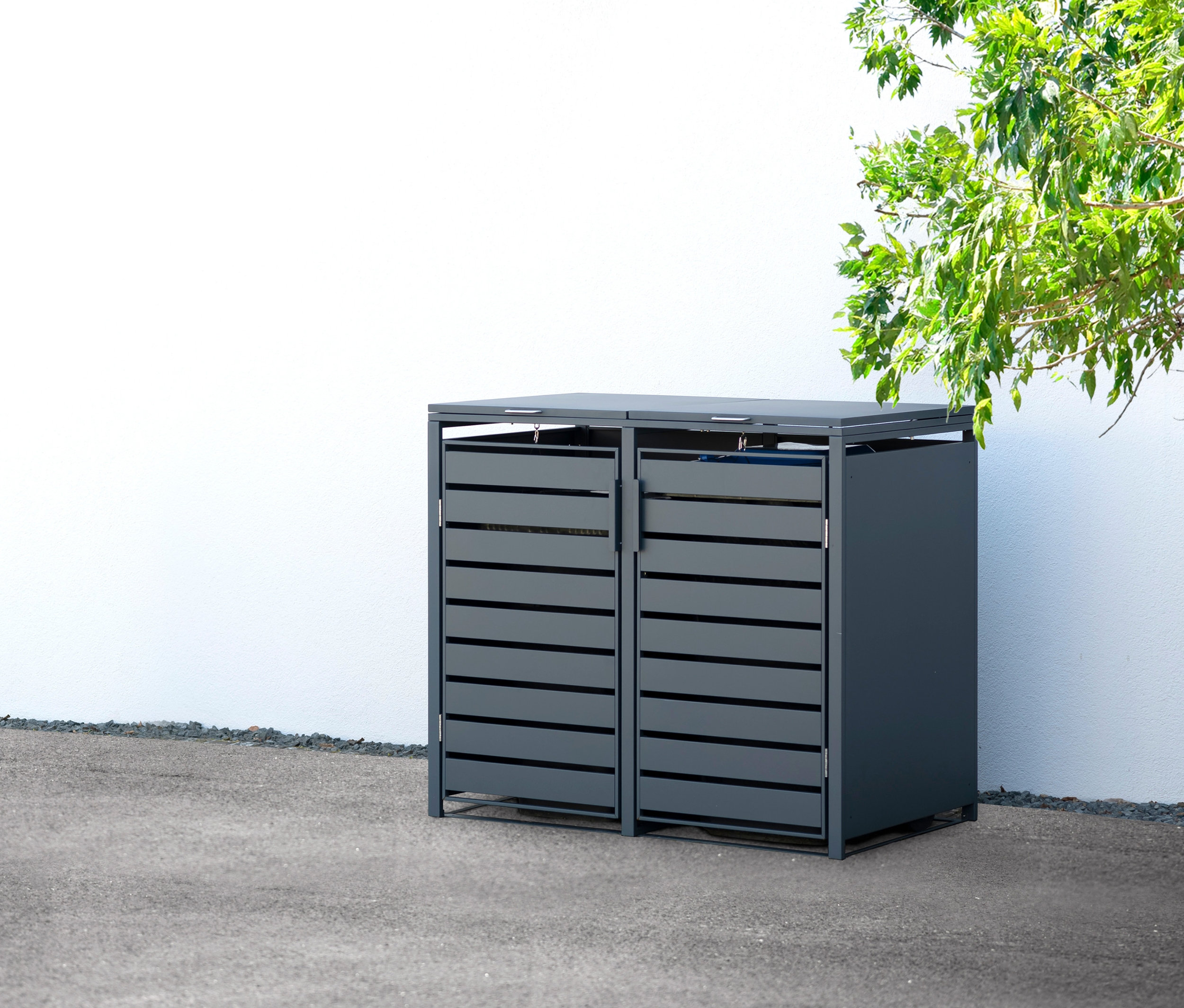 Eine Mülltonnenbox aus Stahl für 2 Mülltonnen steht draußen vor einer weißen Wand.