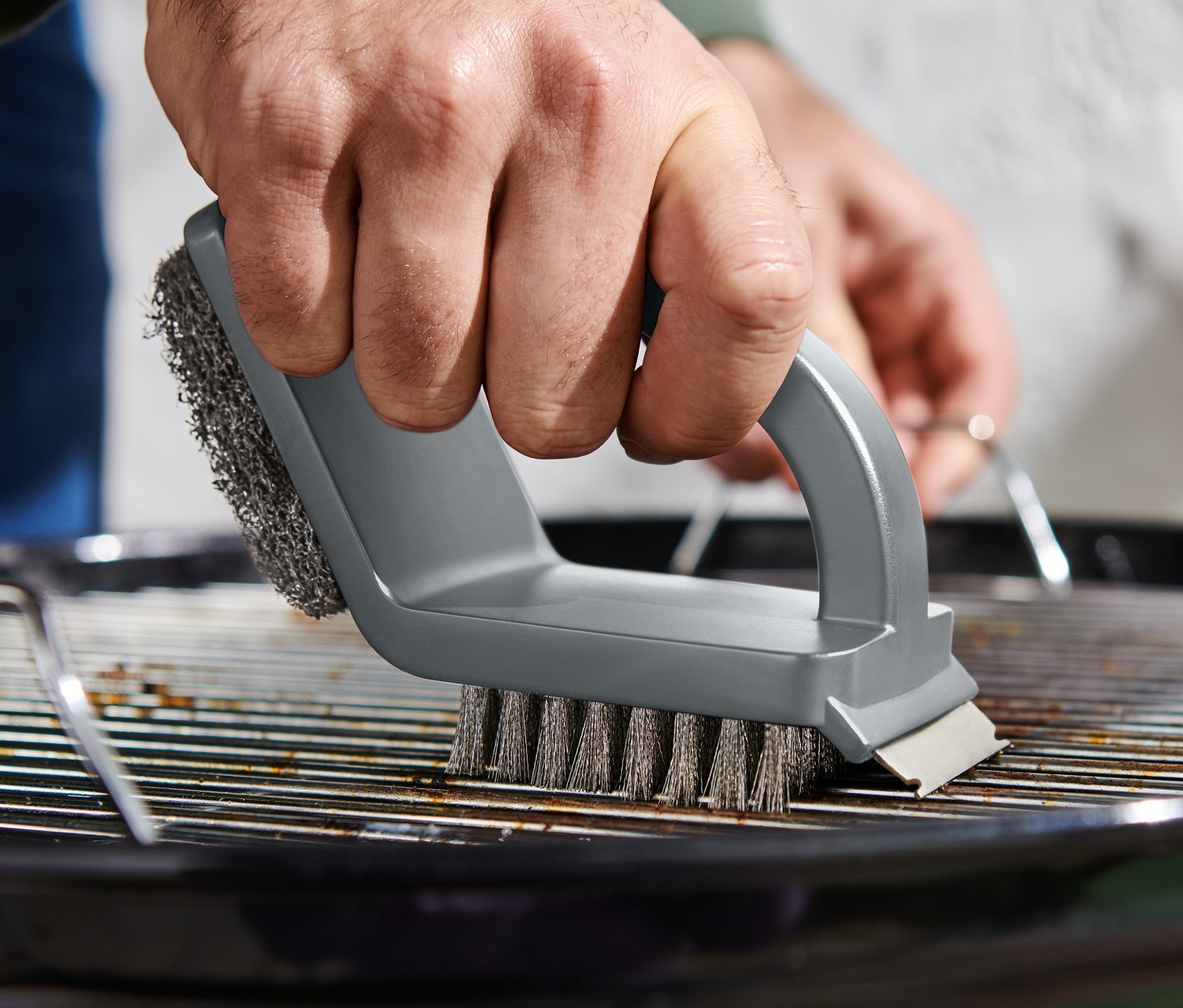Mann reinigt Grillrost mit 3-in-1-Reinigungsbürste.
