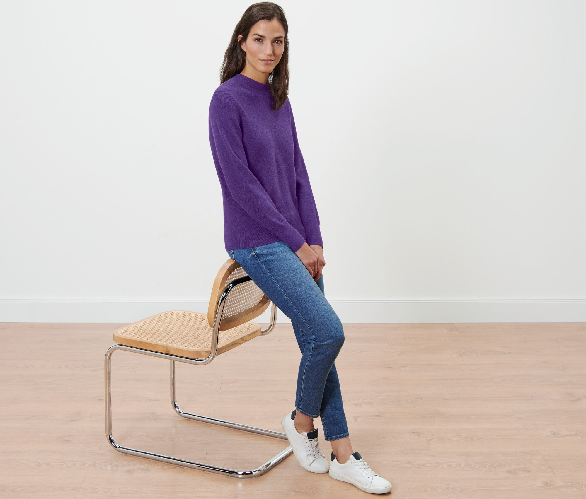 Frau sitzt auf einem Stuhl und trägt einen violetten Feinstrickpullover.