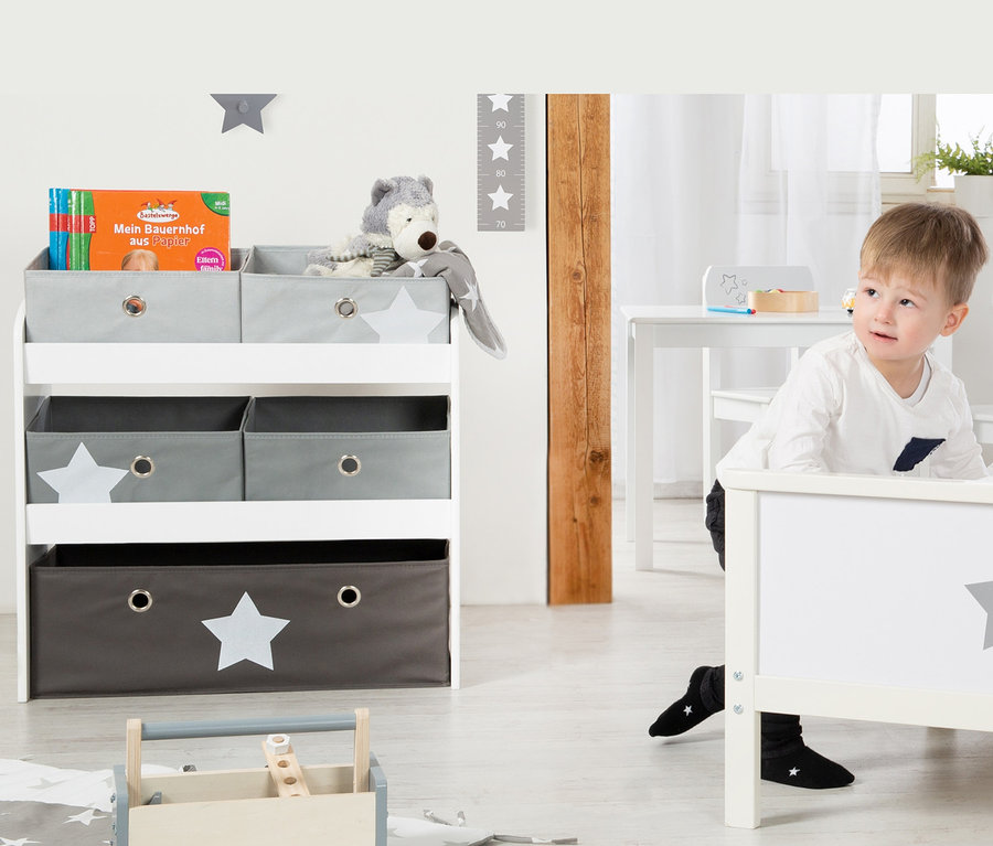 Junge lehnt an weißem Bett mit grauem Stern. Im Hintergrund roba Spielregal "Stars" mit Spielzeug.