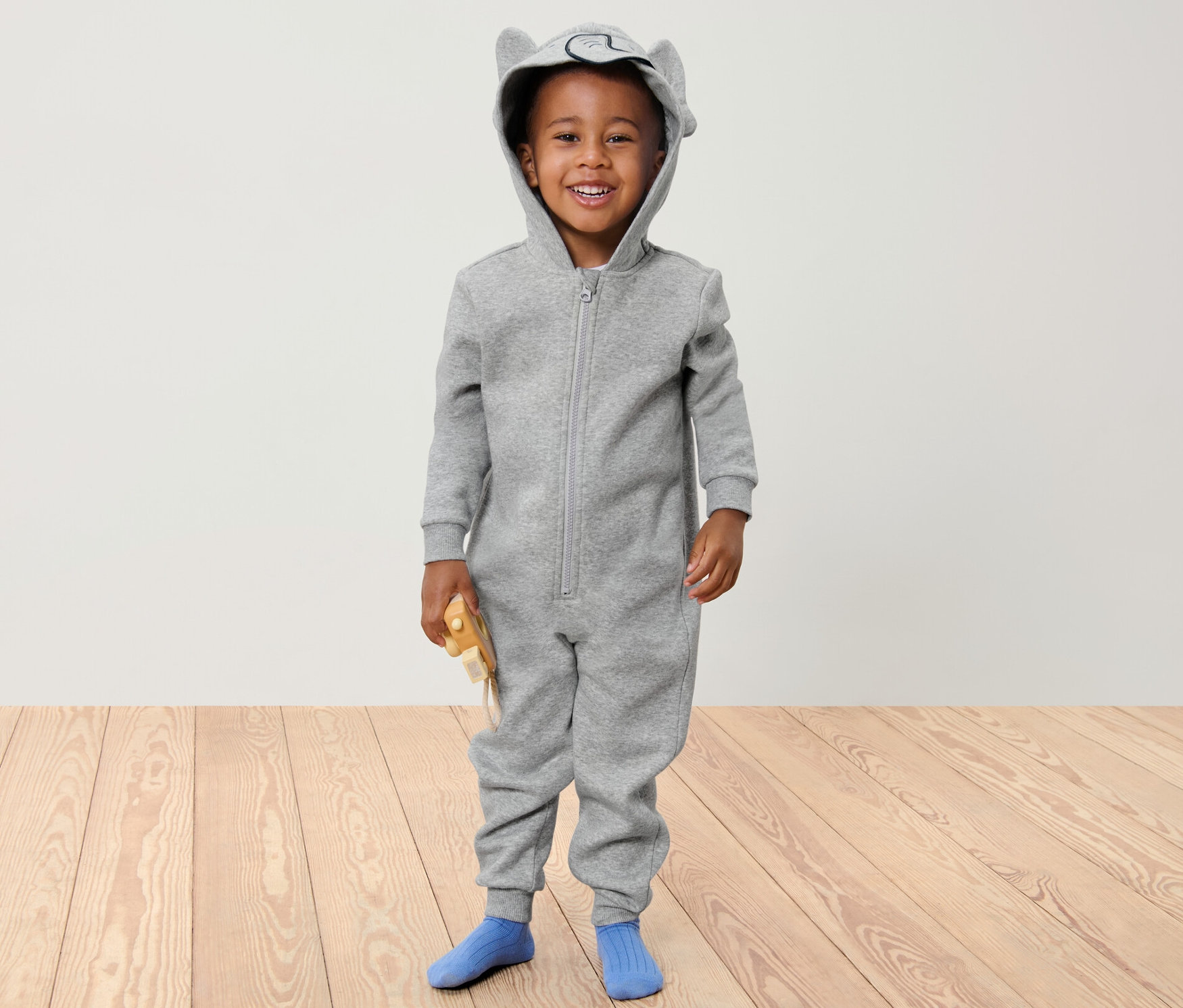 Lächelnder Junge in grauem Kinder-Lounge-Overall mit Kapuze mit Ohren.