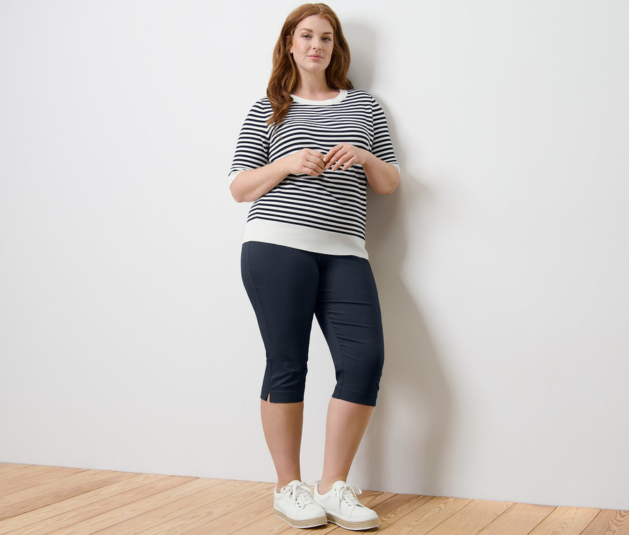 Frau posiert in gestreiftem Feinstrickpullover und dunkelblauer 3/4-Stretchhose.