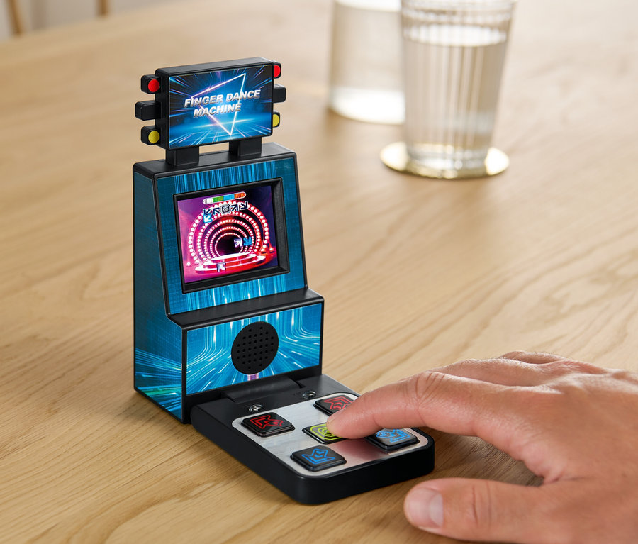 Eine Hand spielt Fingertanzmaschine auf einem Tisch neben einem Glas Wasser.