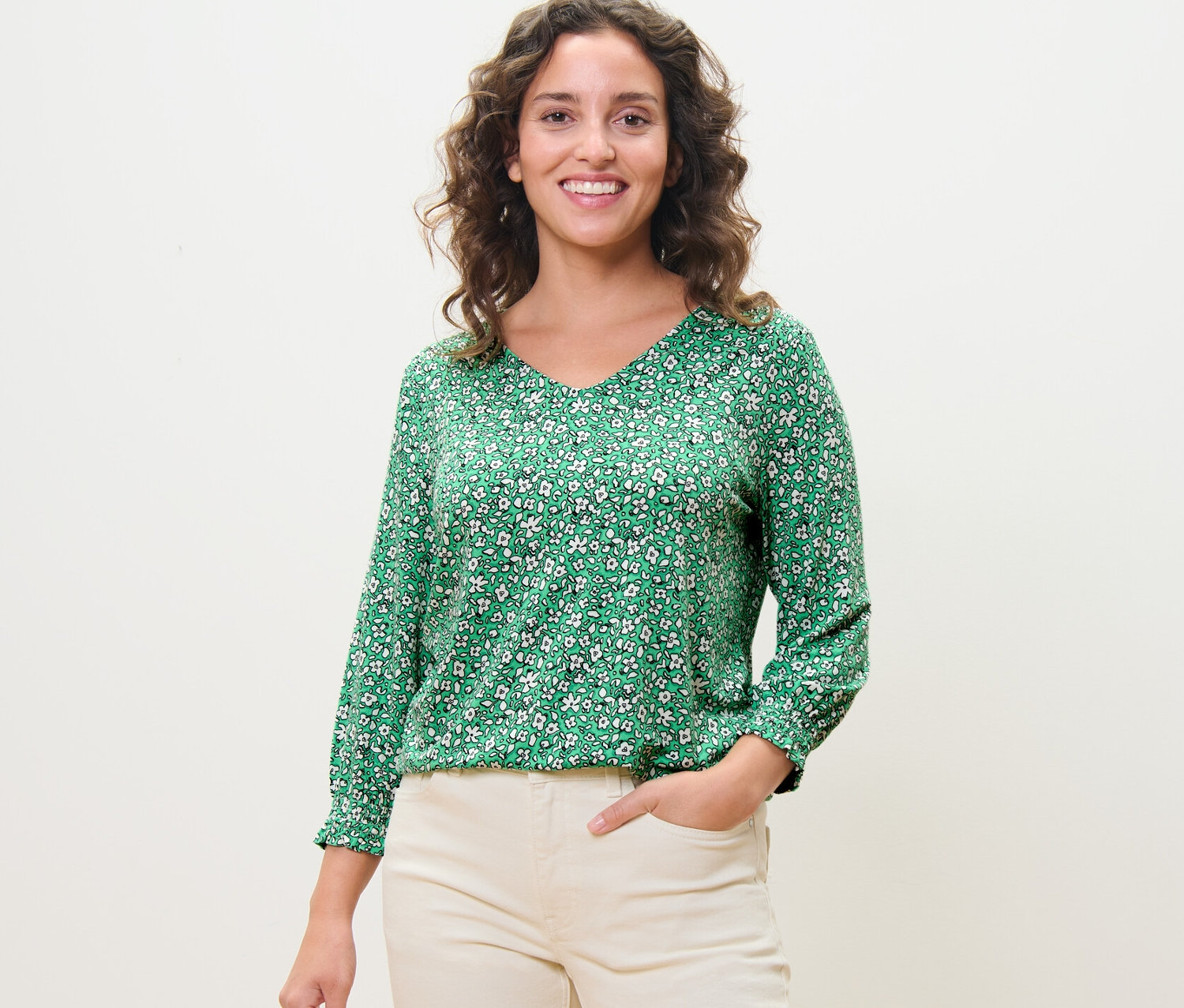 Frau posiert in einem grünen, bedruckten Blusenshirt.