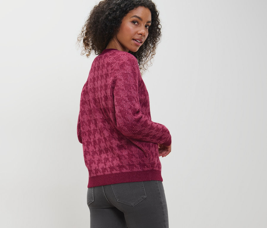 Frau blickt über die Schulter und trägt einen Grobstrick-Cardigan mit Hahnentritt-Jacquard.