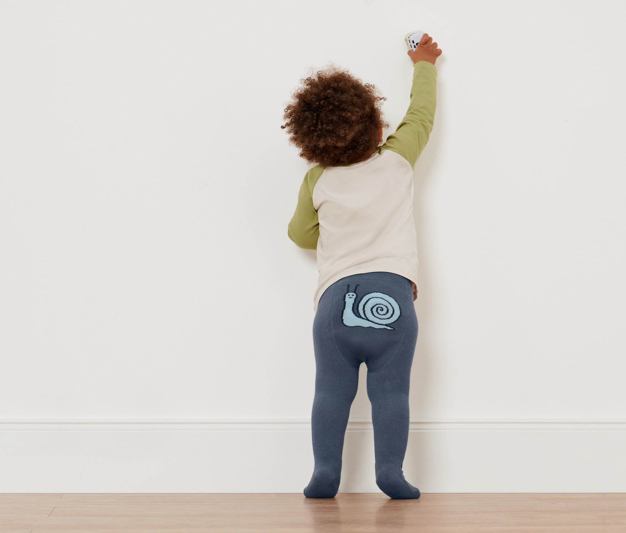 Kleinkind in Strumpfhosen mit Schneckenmotiv greift nach der Wand. Es trägt eine von 4 Baby-und-Kleinkinder-Strumpfhosen.