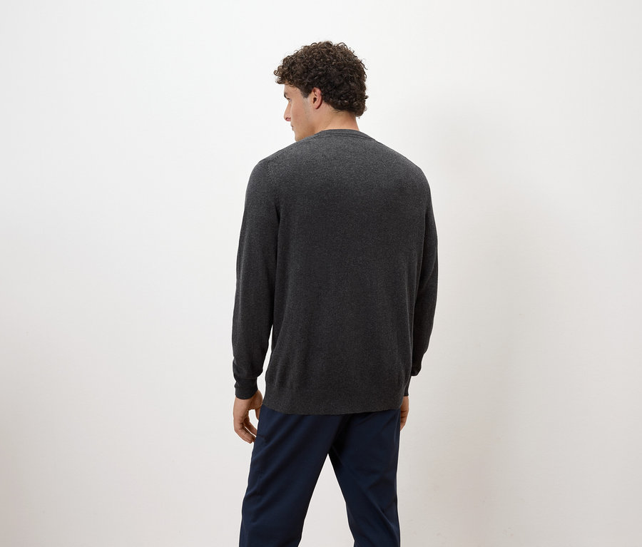 Mann mit lockigem Haar steht mit dem Rücken zur Kamera und trägt einen grauen Pullover und blaue Hosen.